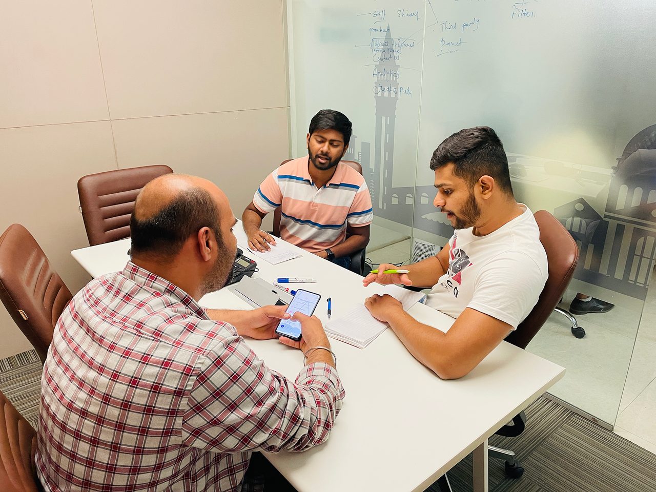 A moderated Pataa usability session: a participant holds the app while two team members watch, a whiteboard of product notes standing behind them.